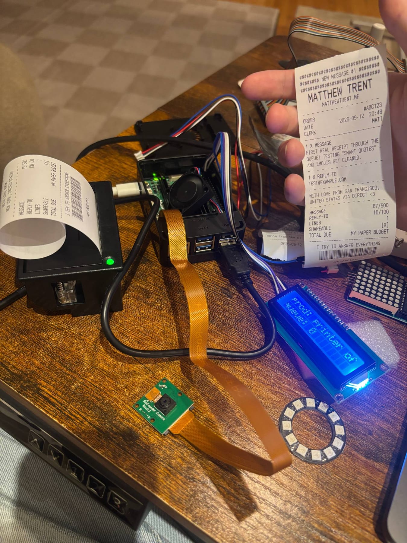 The receipt printer on my desk with a receipt coming out, next to a Raspberry Pi, its LCD and camera, and a printed receipt held up to the camera